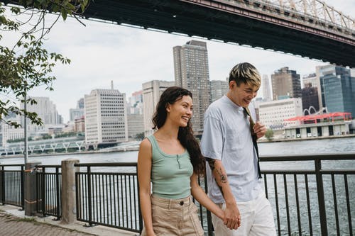 性格开朗的年轻民族夫妇手牵着手，走在市中心河附近 · 免费素材图片