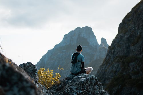 后视图的男子坐在岩石上的灰色t恤的照片 · 免费素材图片