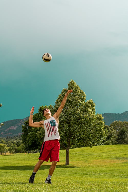 白色背心和蓝色短裤站在绿草地上玩足球的人 · 免费素材图片
