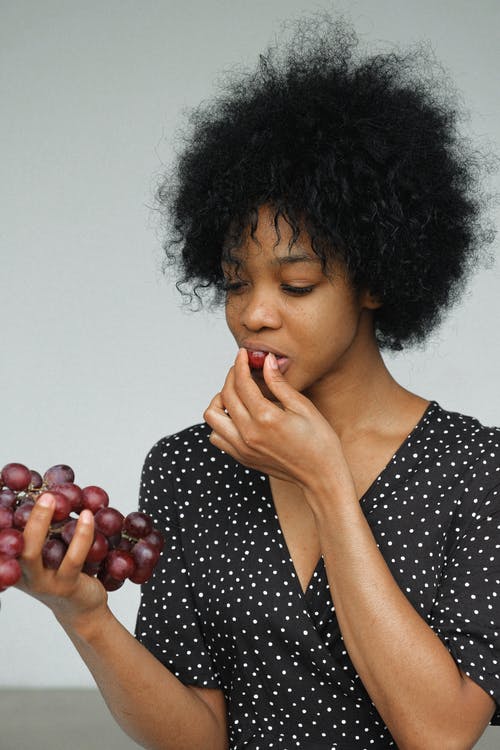 黑色和白色的波尔卡圆点衬衫，拿着和吃葡萄的女人 · 免费素材图片