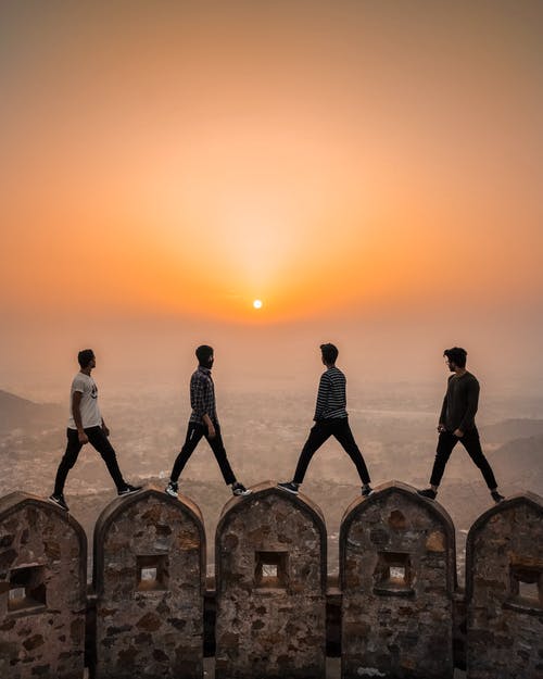 四名男子站在拱形的石墙上，以城市上空的夕阳 · 免费素材图片