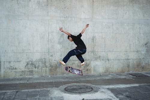 年轻人与混凝土墙附近沙井上跳滑板 · 免费素材图片