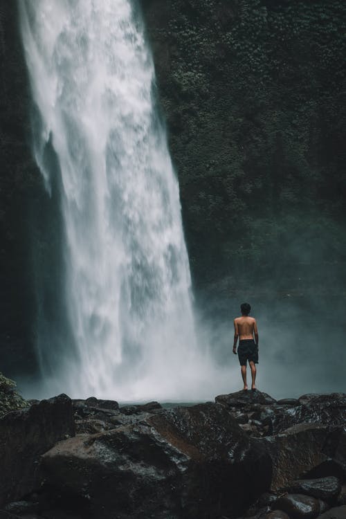站在瀑布附近的岩石上的人 · 免费素材图片
