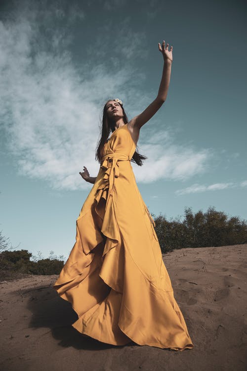 黄色的裙子站在蓝天下的棕色沙滩上的女人 · 免费素材图片