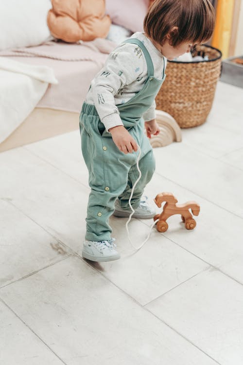 白色长袖上衣和粗蓝布长裤的孩子在白色地板上玩木制玩具 · 免费素材图片