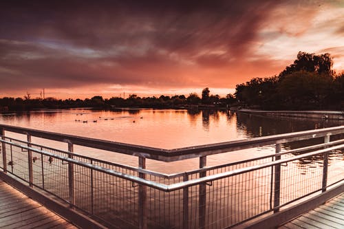 日落期间水体附近的白色金属栏杆 · 免费素材图片