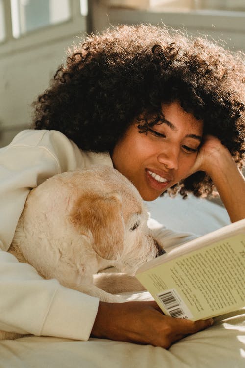 休息和读与狗的快乐的黑人妇女在床上 · 免费素材图片