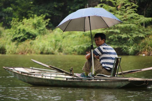 男子坐在灰色的木船上 · 免费素材图片