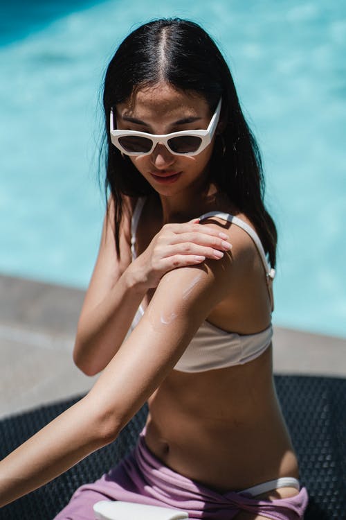 女人在游泳池边晒日光浴时在肩膀上涂防晒霜 · 免费素材图片