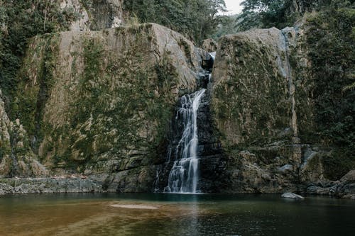 纯净池塘附近的崎mountains山脉之间的快速瀑布 · 免费素材图片
