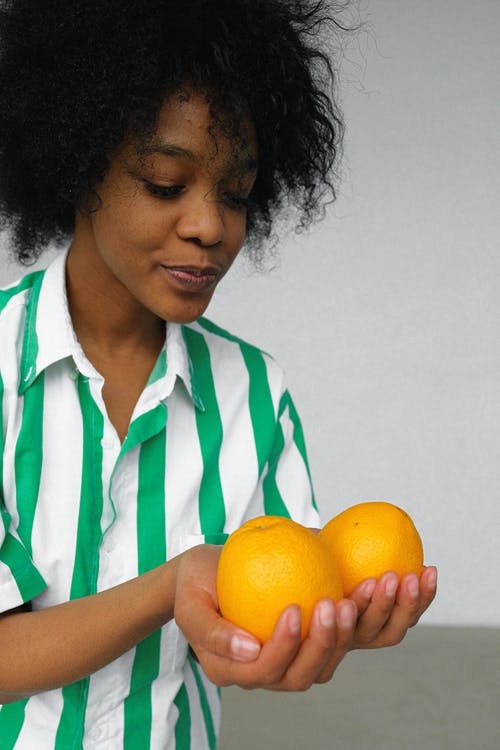 拿着橙色水果的白色和绿色条纹衬衫的女人的照片 · 免费素材图片