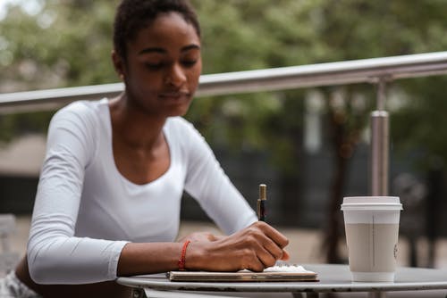 黑人妇女与咖啡和笔在露台上 · 免费素材图片