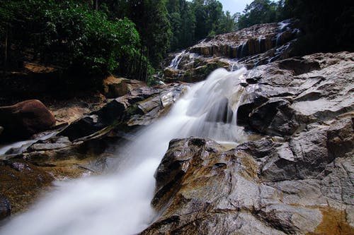 树木环绕的岩石上的瀑布 · 免费素材图片