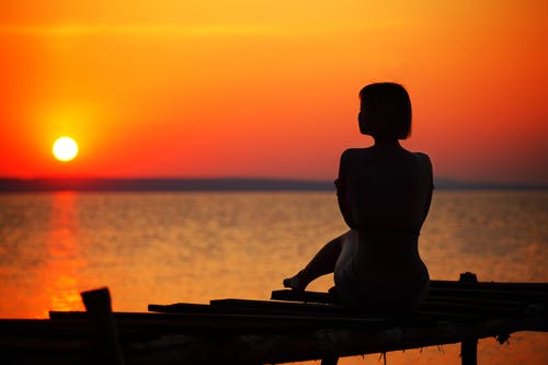 女人在日落时分坐在码头上的剪影 · 免费素材图片