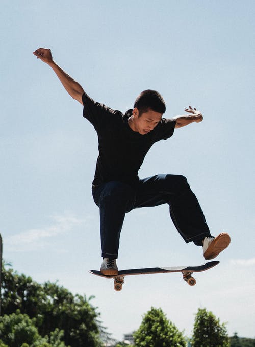 自信的年轻人，在阳光明媚的日子在滑板上跳高 · 免费素材图片