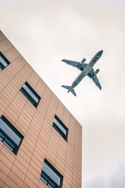 棕色的高层建筑，在天空中显示蓝色飞机的低角度摄影 · 免费素材图片