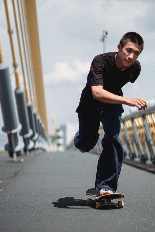 快乐的年轻人骑滑板沿着现代斜拉桥的一条腿上 · 免费素材图片