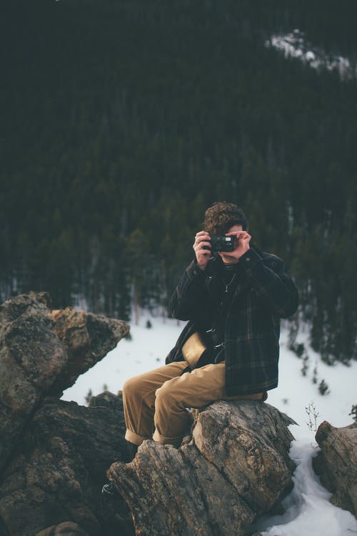 坐在岩石上使用相机的人 · 免费素材图片