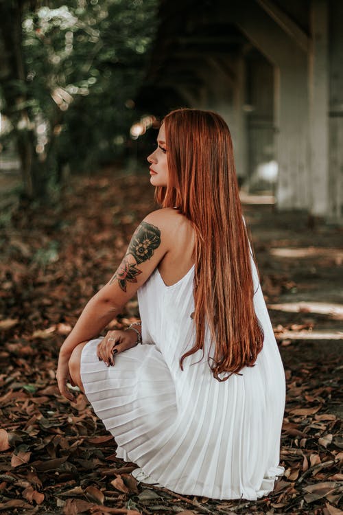 白色连衣裙坐在地上用干树叶的女人 · 免费素材图片