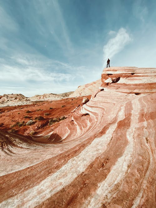 站在蓝天下的棕色岩石形成上的人 · 免费素材图片
