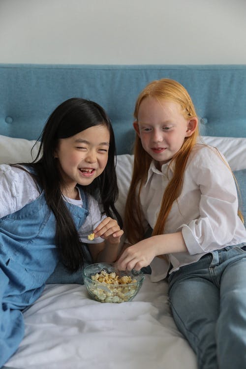 满足多种族的女孩在家里舒适的床上吃爆米花 · 免费素材图片