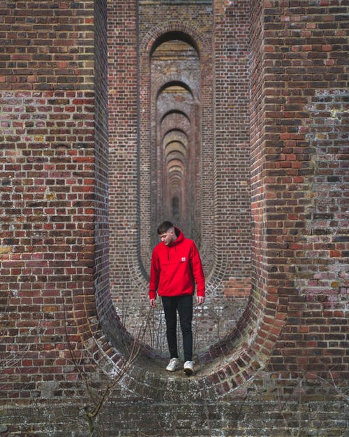 站在砖墙上的红色外套的男人 · 免费素材图片