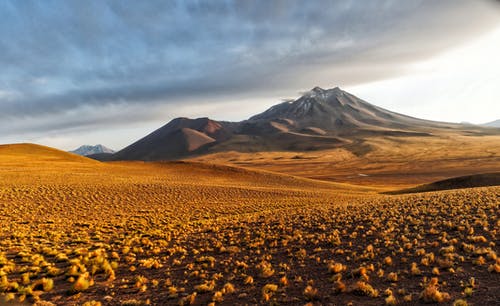 多云的天空下山附近的棕色领域 · 免费素材图片