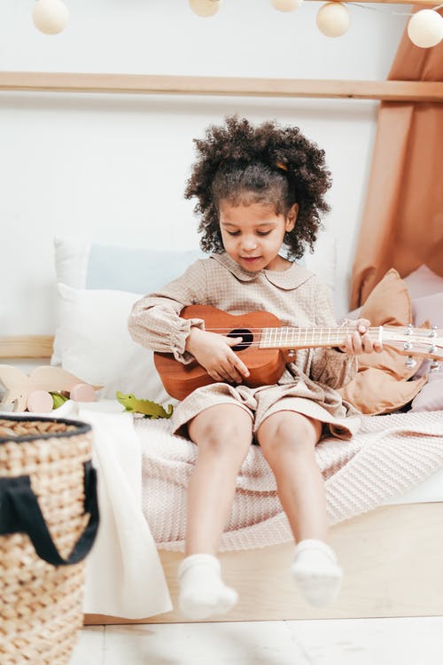 一个穿着高领长袖连衣裙的女孩在玩棕色原声吉他 · 免费素材图片