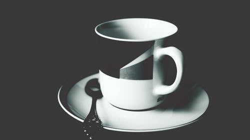 白色和黑色陶瓷茶杯放在白色陶瓷圆盘上，不锈钢勺在上面 · 免费素材图片