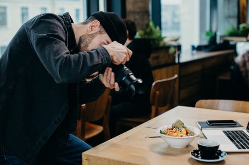 在餐厅内的桌子上的食物拍照的人 · 免费素材图片