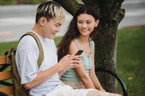 微笑多种族的夫妇浏览智能手机和在公园里交流 · 免费素材图片