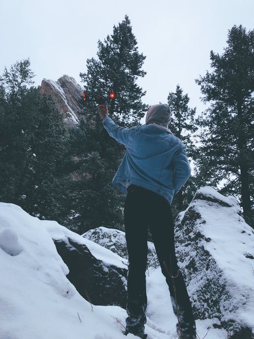 穿着蓝色夹克和黑色的裤子，站在雪地上抱着无人机的人 · 免费素材图片