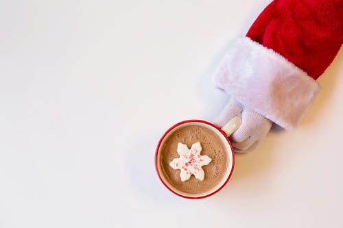 大杯巧克力饮料，上面放着雪花状饼干，一个圣诞老人服的人拿着 · 免费素材图片