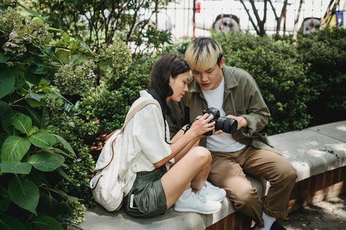 亚洲夫妇在郁郁葱葱的公园中使用现代摄影相机 · 免费素材图片