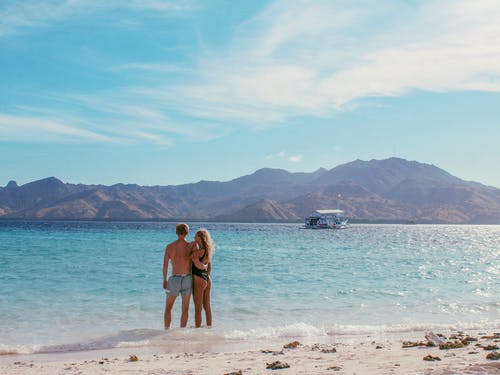 男人和女人站在海滩岸边 · 免费素材图片
