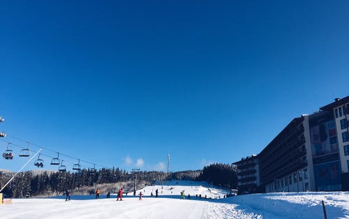 人们在白雪皑皑的滑雪山上，左边有电梯，右边有旅馆 · 免费素材图片
