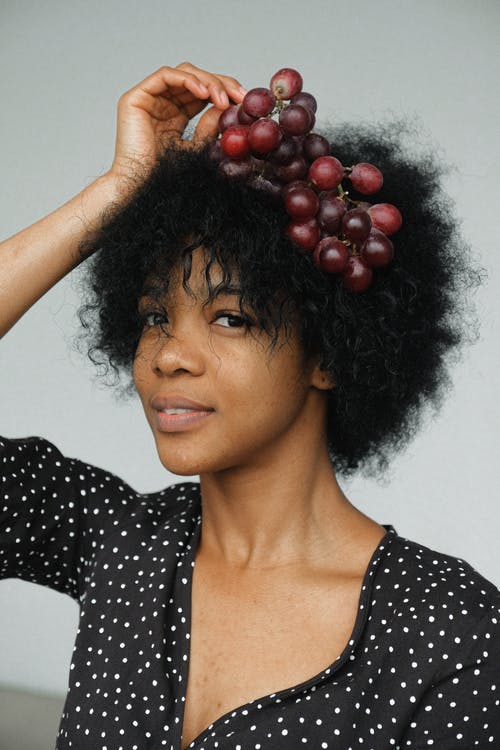 黑色和白色的圆点衬衫，拿着葡萄在她的头的女人的肖像照片 · 免费素材图片