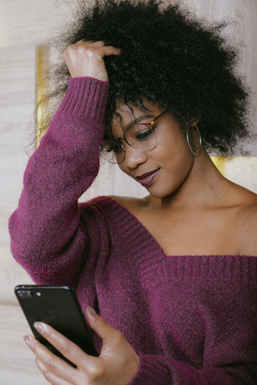 拿着黑色智能手机的紫色毛衣的女人 · 免费素材图片