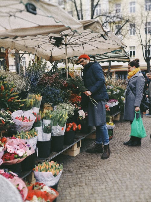 黑色外套和蓝色牛仔牛仔裤买花的男人 · 免费素材图片