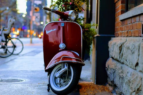 红色piaggio Vespa小型摩托车停在灰色和红色的混凝土建筑旁边 · 免费素材图片