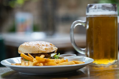 汉堡和薯条与啤酒杯旁边 · 免费素材图片