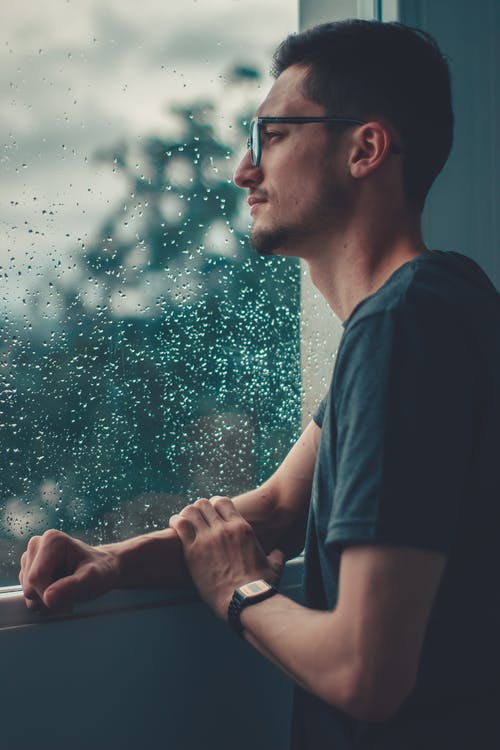 男子斜倚在玻璃窗上看着雨 · 免费素材图片