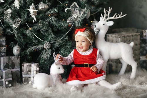 宝贝女孩穿着圣诞老人的衣服坐在圣诞树旁 · 免费素材图片