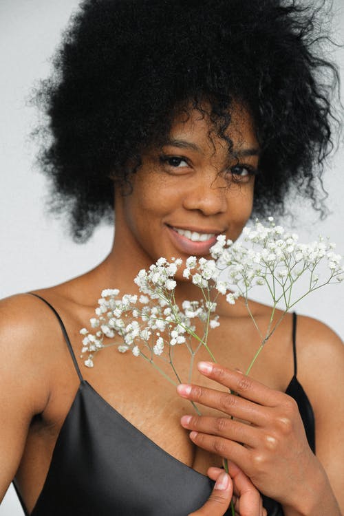 微笑的女人，在拿着白色花的黑色意大利面条皮带顶部的肖像照片 · 免费素材图片