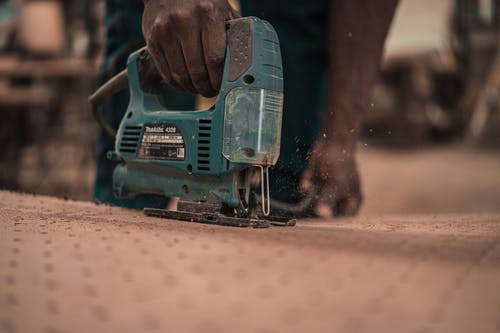 男子手持蓝绿色和黑色电动工具 · 免费素材图片