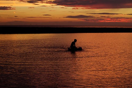 人在日落时在水体上的剪影 · 免费素材图片