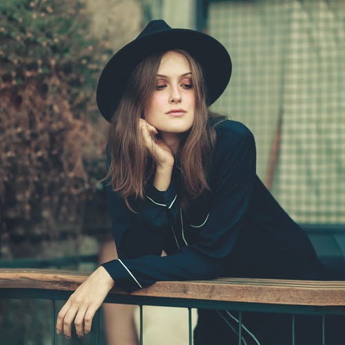 穿黑夹克的女人斜倚在木栏杆上 · 免费素材图片