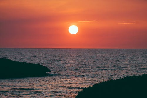 日落期间海上岩石形成的剪影 · 免费素材图片