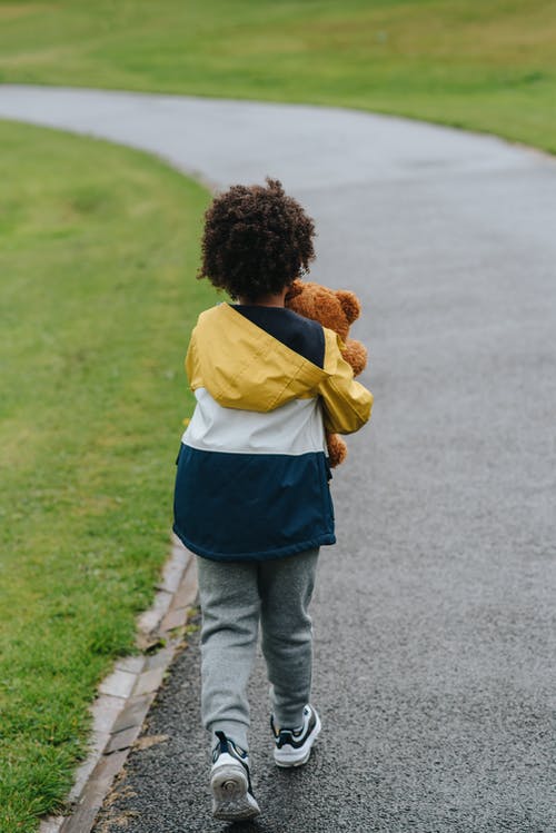 不可识别的民族男孩与玩具熊漫步在人行道上 · 免费素材图片