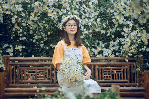 女孩坐在长凳上用雏菊花束 · 免费素材图片